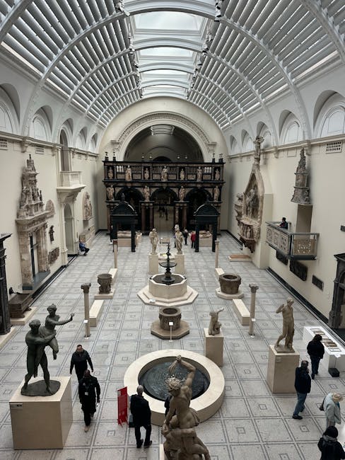 Interior view of a historic museum hall featuring high, arched glass ceilings and white walls with intricate architectural details. The spacious room displays various classical sculptures on pedestals, surrounding a central fountain with a sculpted figure, and additional statues and decorative stonework along the walls. The polished tiled floor reflects the lighting, showcasing a clean and well-maintained surface. Several visitors are walking through the space, indicating a tidy and hygienic environment. The image highlights the importance of surface cleaning and maintenance in a cultural heritage setting, consistent with professional cleaning practices by South Kensington Cleaners.