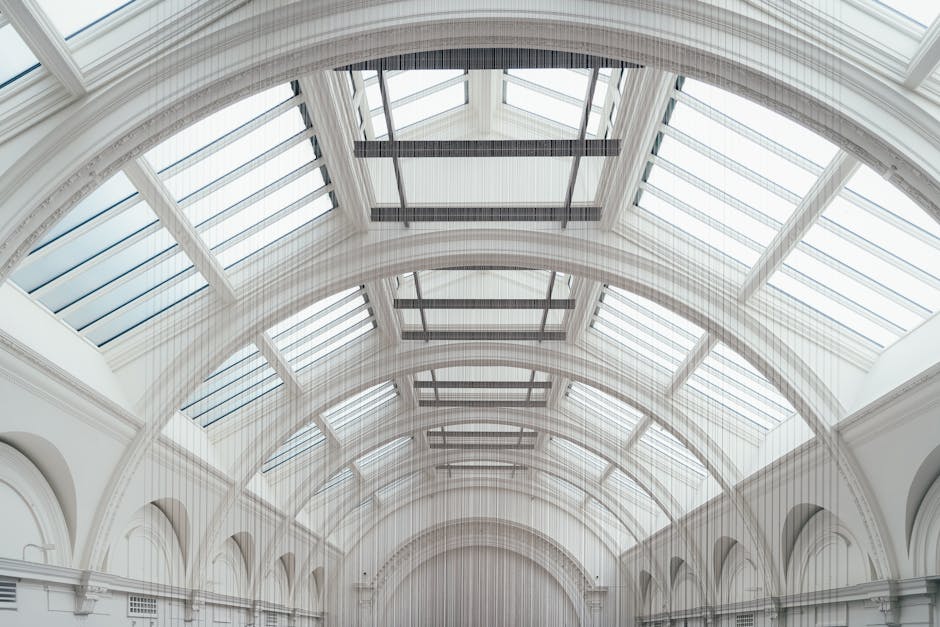 Interior view of a historic museum hall featuring high, arched glass ceilings and white walls with intricate architectural details. The spacious room displays various classical sculptures on pedestals, surrounding a central fountain with a sculpted figure, and additional statues and decorative stonework along the walls. The polished tiled floor reflects the lighting, showcasing a clean and well-maintained surface. Several visitors are walking through the space, indicating a tidy and hygienic environment. The image highlights the importance of surface cleaning and maintenance in a cultural heritage setting, consistent with professional cleaning practices by South Kensington Cleaners.
