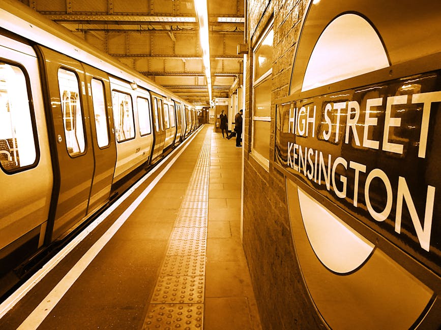 The image depicts a clean, well-maintained platform at South Kensington underground station, part of the London Underground network. A yellow train with closed doors is stationed along the platform, w