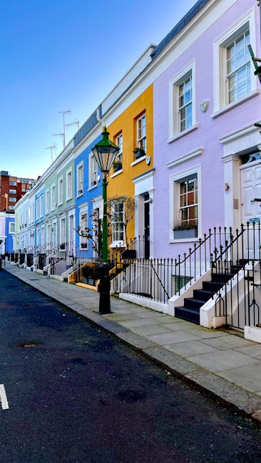 A row of vibrantly colored terraced houses along a quiet street in South Kensington, with pastel facades painted in shades of blue, yellow, and pink. Each house features white-framed sash windows, black wrought iron railings, and small front steps leading to main entrances. A classic black lamppost stands near the sidewalk, and the street appears clean and well-maintained under bright daylight. Visible elements include potted plants on window sills and a clear blue sky, highlighting the charming and picturesque residential area. South Kensington Cleaners specializes in surface cleaning, deep cleaning, and sanitisation services for residential spaces, ensuring homes in the SW7 area remain pristine and hygienic.